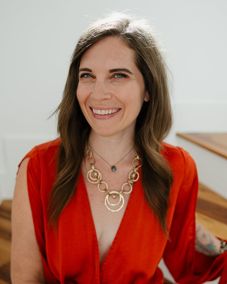 Lindsey Means smiling, wearing a red wrap top and a gold necklace